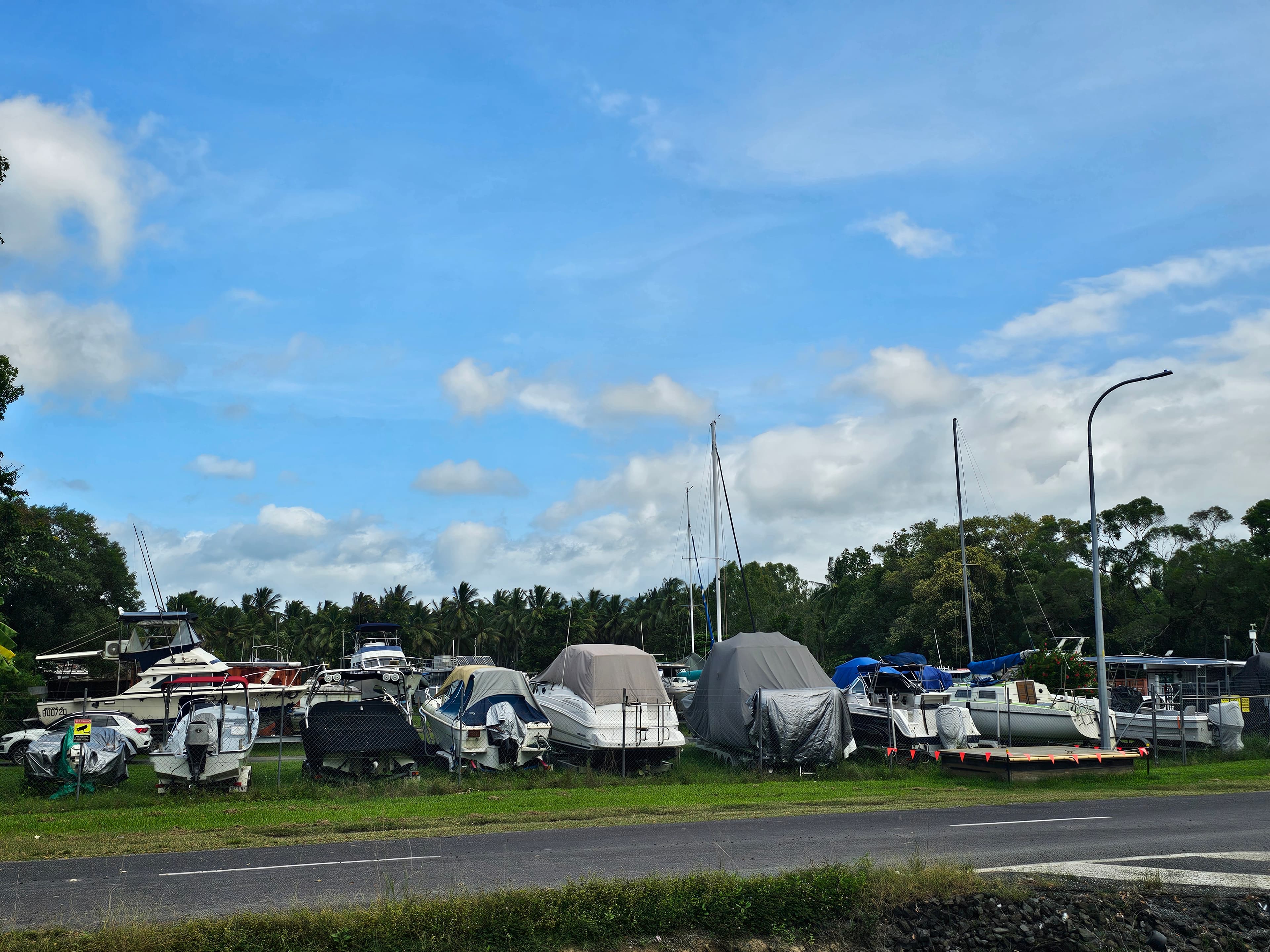 A row of trailer boats, some under covers, stored along the yard's road frontage