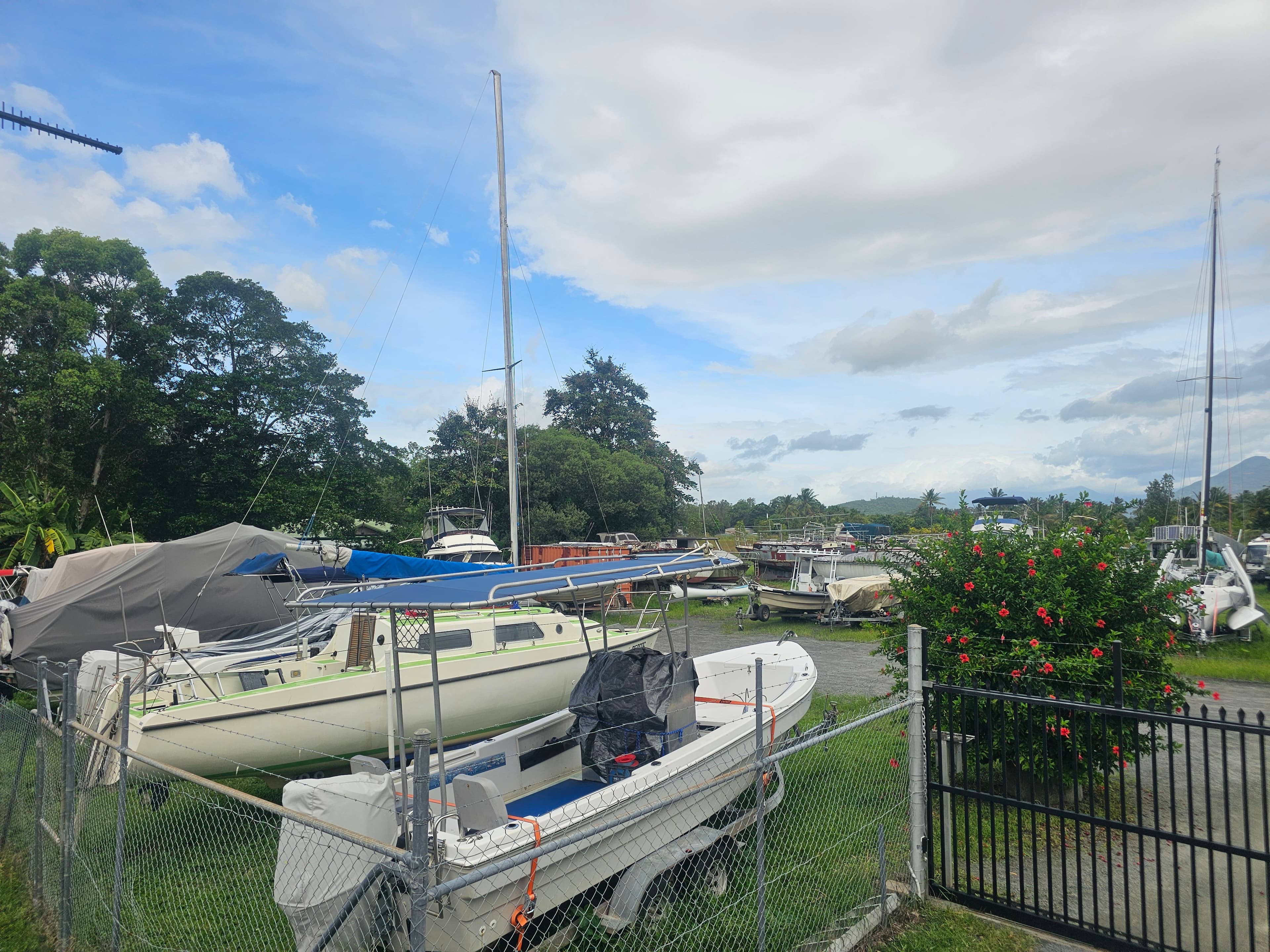 A yacht and trailer boats stored side by side behind the yard's security fencing